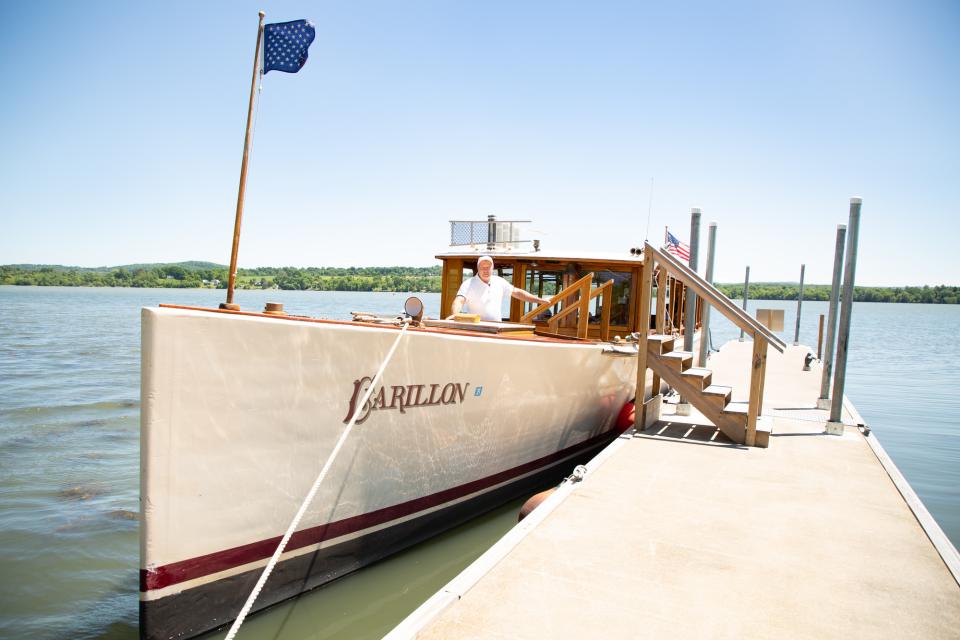 A sleek 1920's style boat sits next to a dock with the captain standing at the bow.