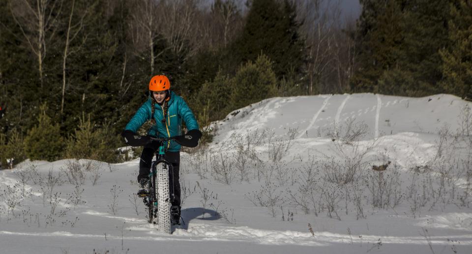 Woman rides fat tire bike down a gentle hill of soft snow.
