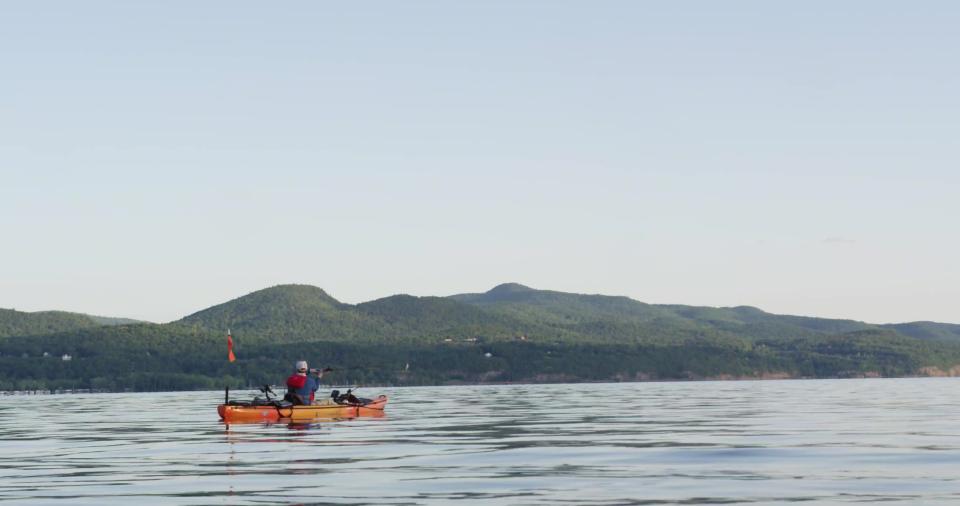 Brian sits on his kayak with the mountains as a backdrop in the distance
