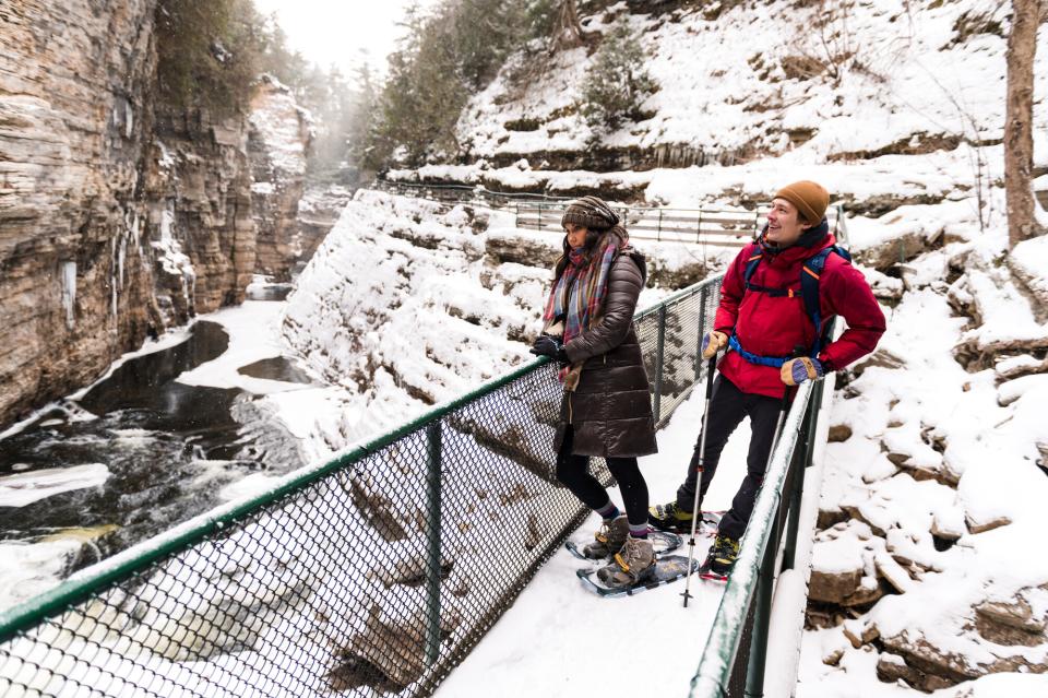 Two people stand on a bridge that spans the width of the chasm, smiling in awe of the incredibly large chasm walls.