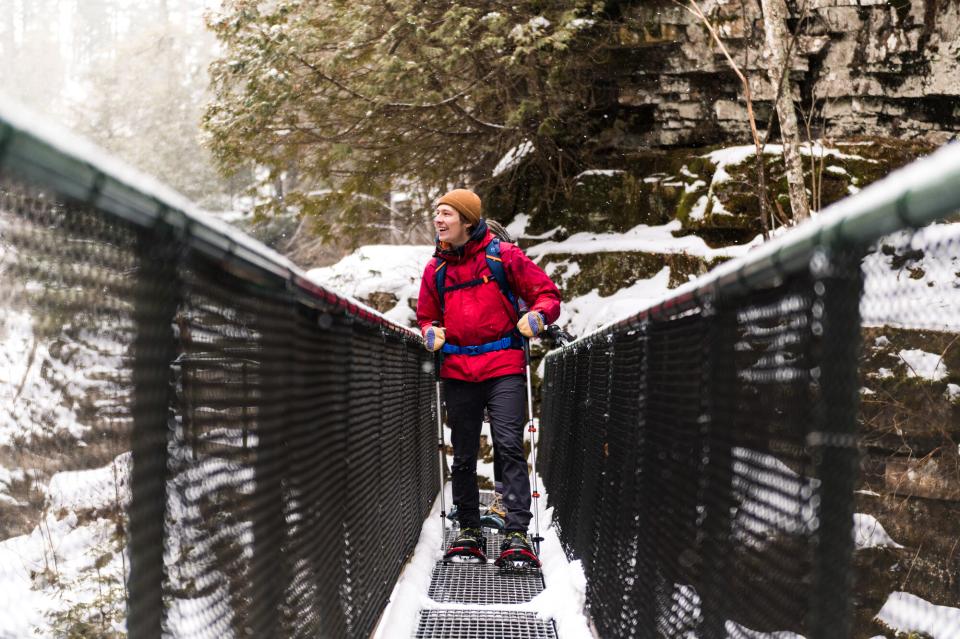 A man stands on a metal bridge laughing at the enormity of the ice formations around him.