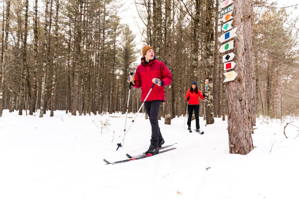 A man and a woman reach an intersection in the cross country ski trails, indicated by numerous signs designating different paths they could choose.