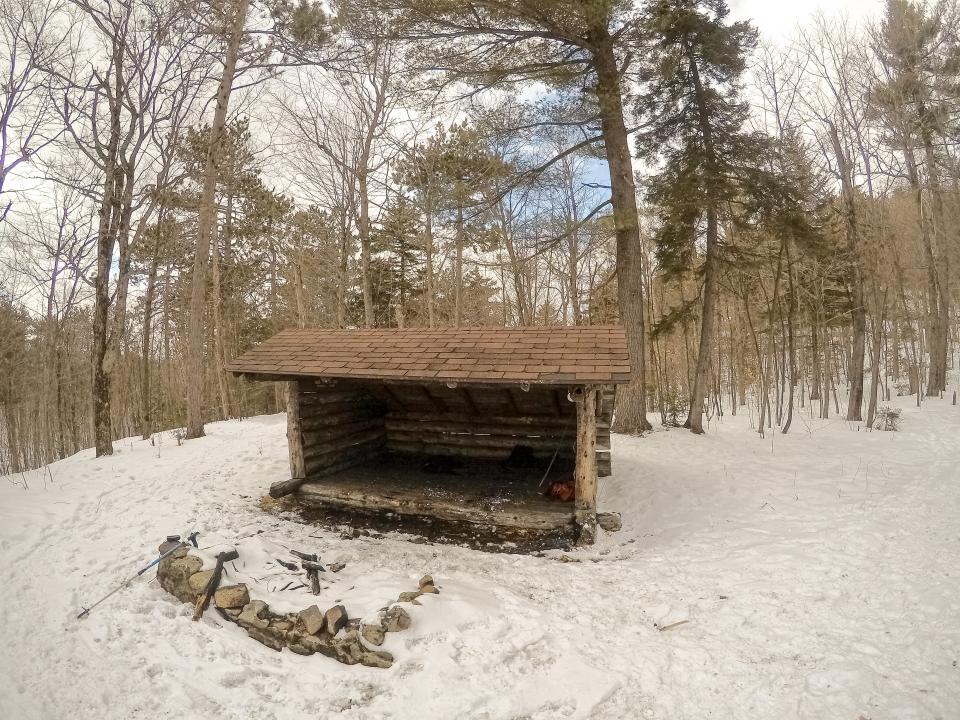A wooden leanto in a snowy forest clearing.