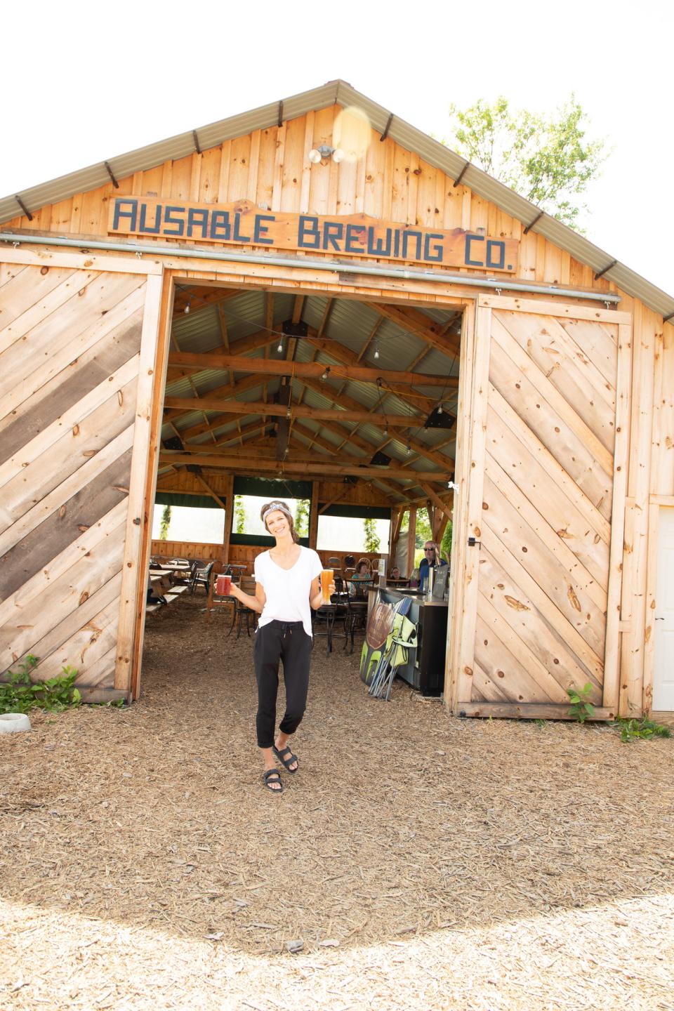 A waitress emerges from a brewery built in a barn on a sunny day.
