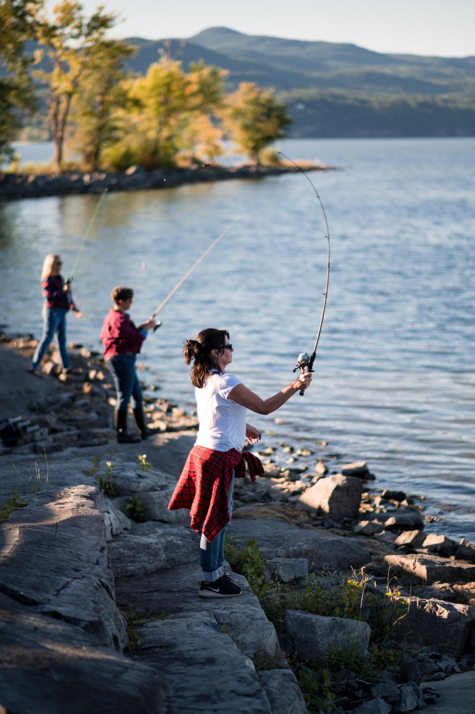 Women casting fishing lines from a rocky lake shoreline.