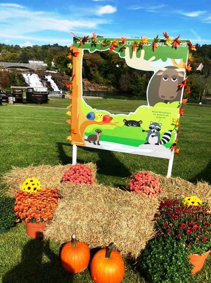 A selfie photo frame decorated with animals and leaves stands behind hay bales, mums, and pumpkins.