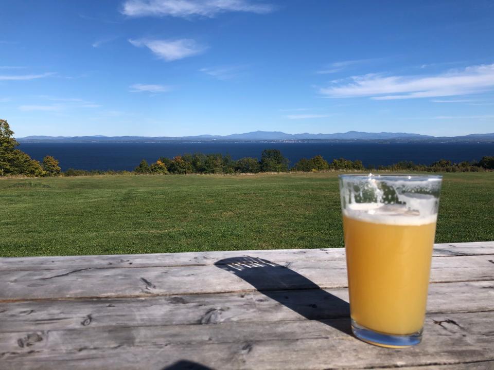 a pint of beer sits on a picnic table, overlooking Lake Champlain.