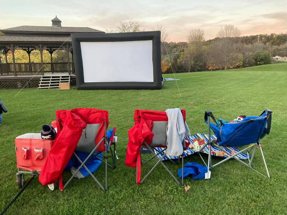 Camping chairs sit on a lawn in front of an inflatable movie screen.