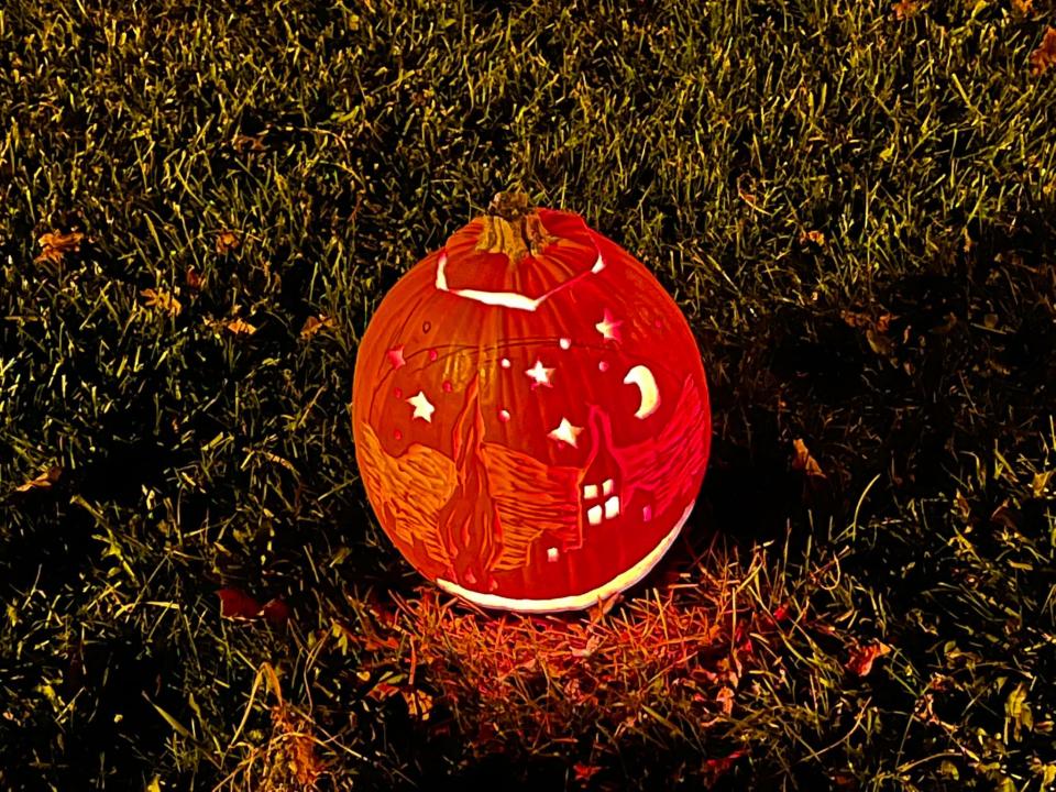 A fanciful carved pumpkin glows on a lawn