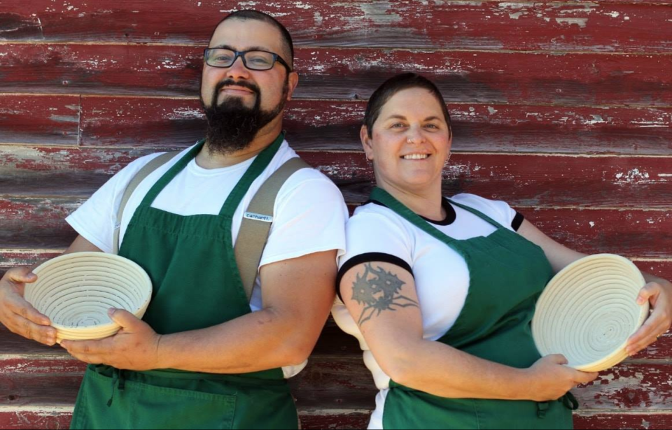 Couple in matching tshirts and green aprons pose with their bread baskets