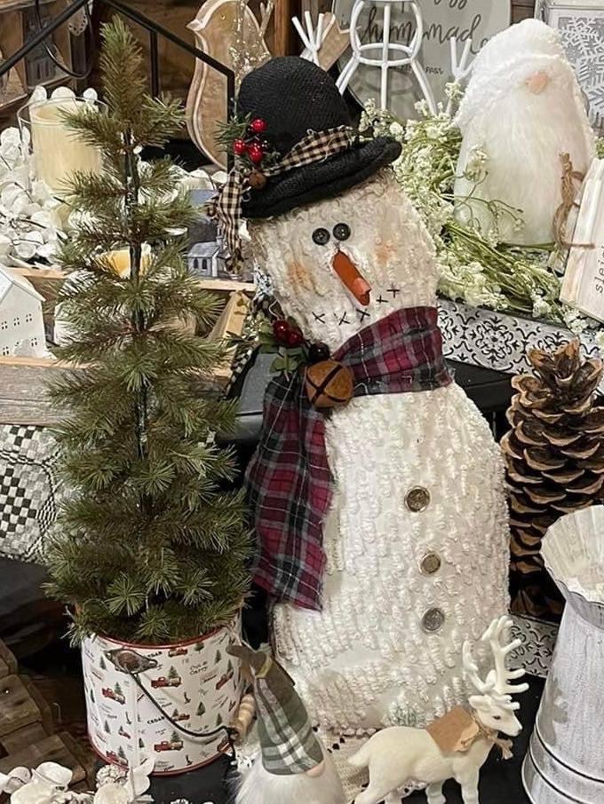 A creatively crafted snowman sits near greens and pinecones in a store display