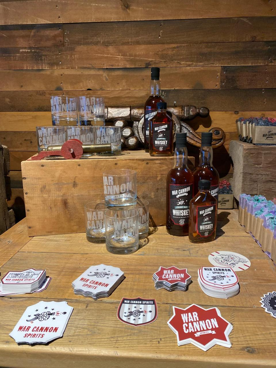 A display of War Cannon Spirits products including spirits, drinking glasses, stickers, and spirit-infused soaps