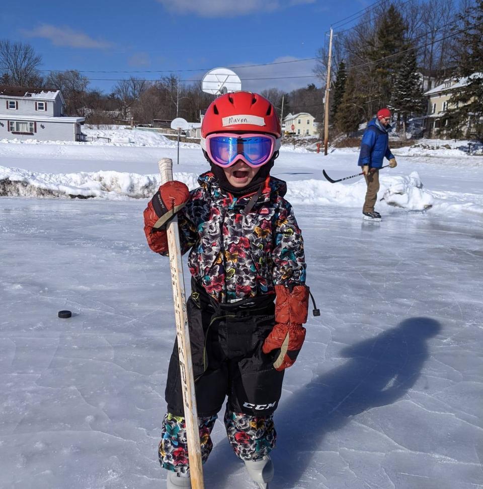 A kid poses with their hockey stick on a small outdoor ice rink