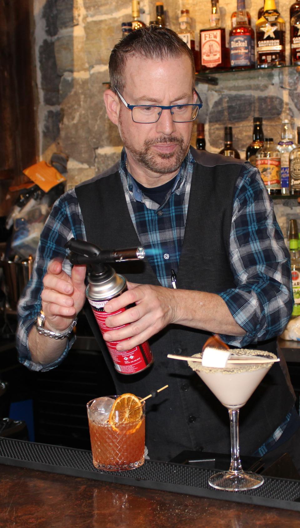 A bartender heats up a marshmallow on a cocktail