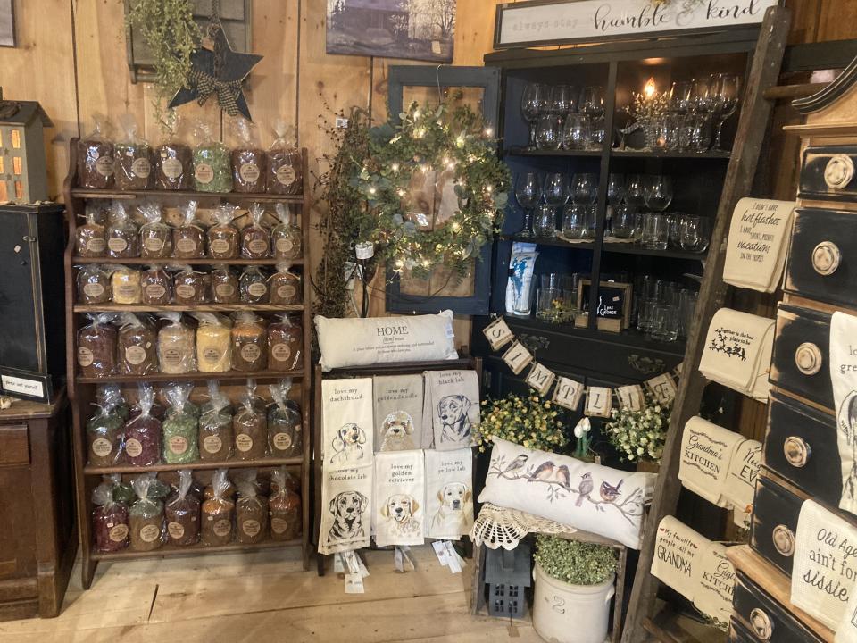 A gift shop display featuring farmhouse decor, including lighted greenery, candles, and tea towels.