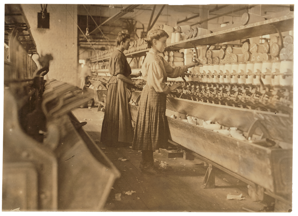 A vintage, sepia-toned photograph of young women at work in a factory in the early 20th century.