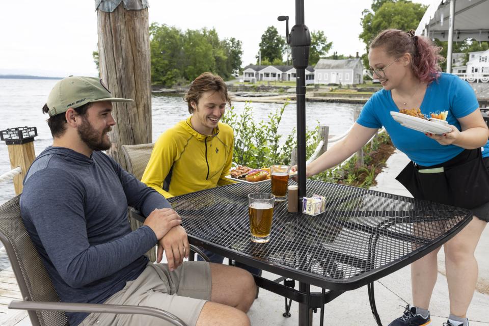 Two people sit at an outdoor table at The Old Dock Restaurant and Marina as a server delivers their order