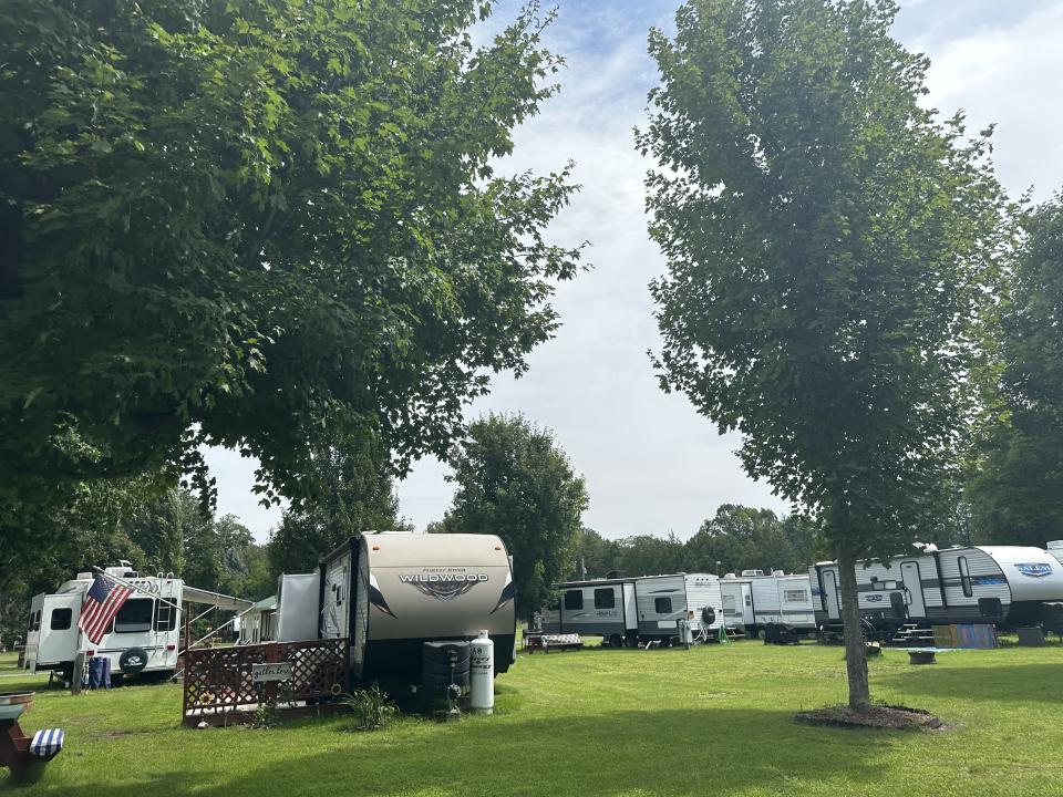 A row of RV's stand in trimmed grass.