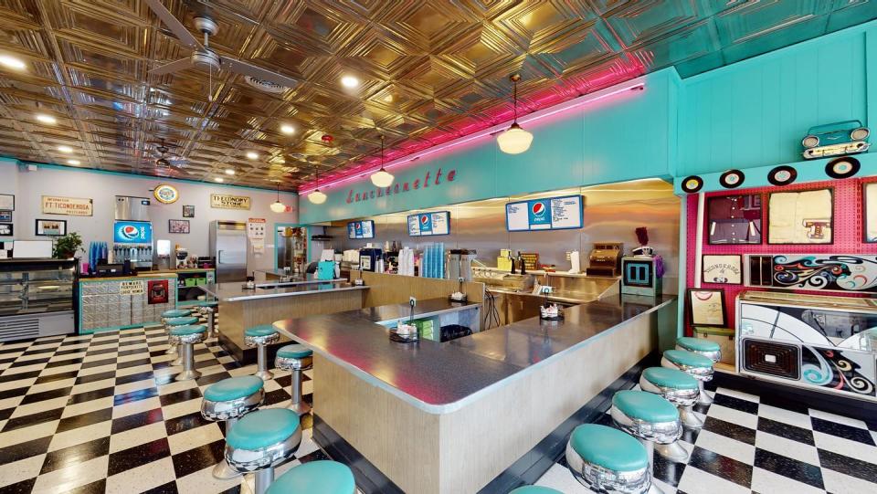The brightly decorated interior of a retro diner, with turquoise walls, pink trim, and black and white checkered floor.
