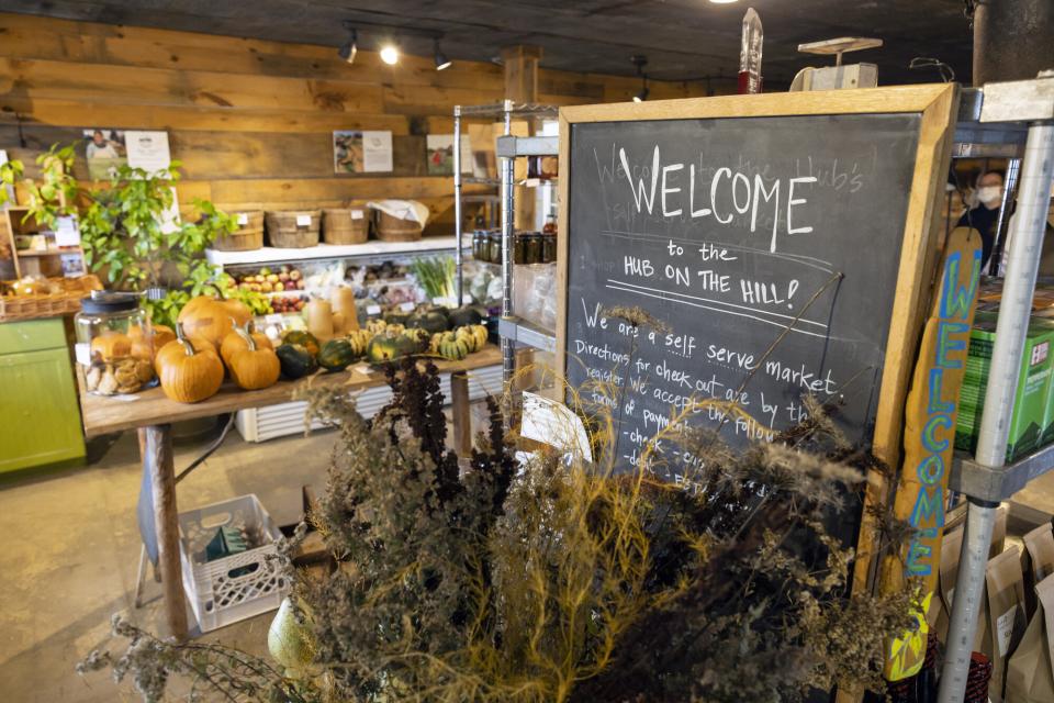 A fall-themed display of corn stalks stand around a chalkboard welcoming visitors to a local fresh produce market.