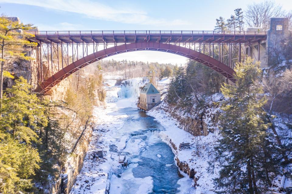 A wide view down into a chasm in winter. A red bridge spans the deep, snowy and icy river.