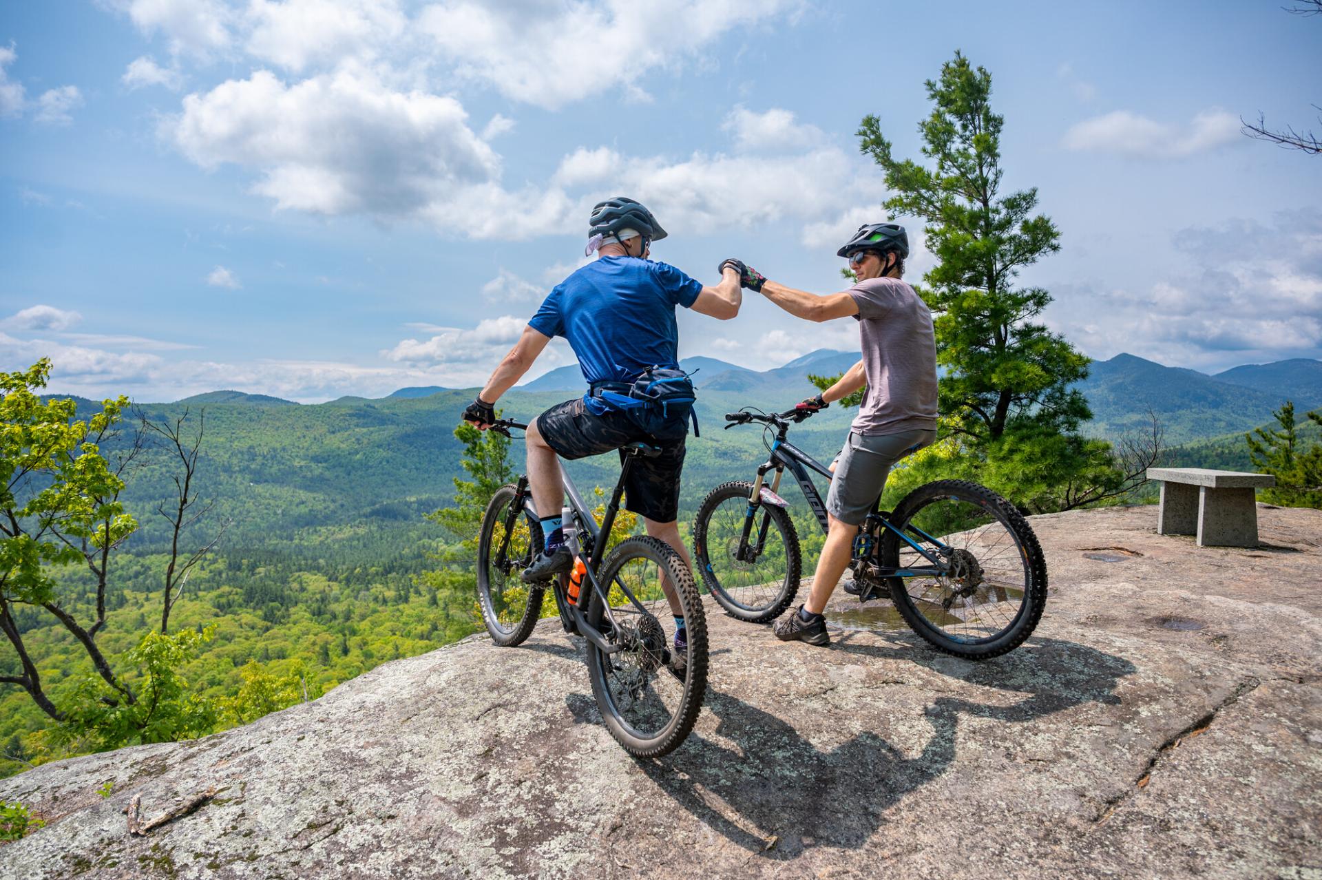 Two mountain bikers fist bump at an overlook
