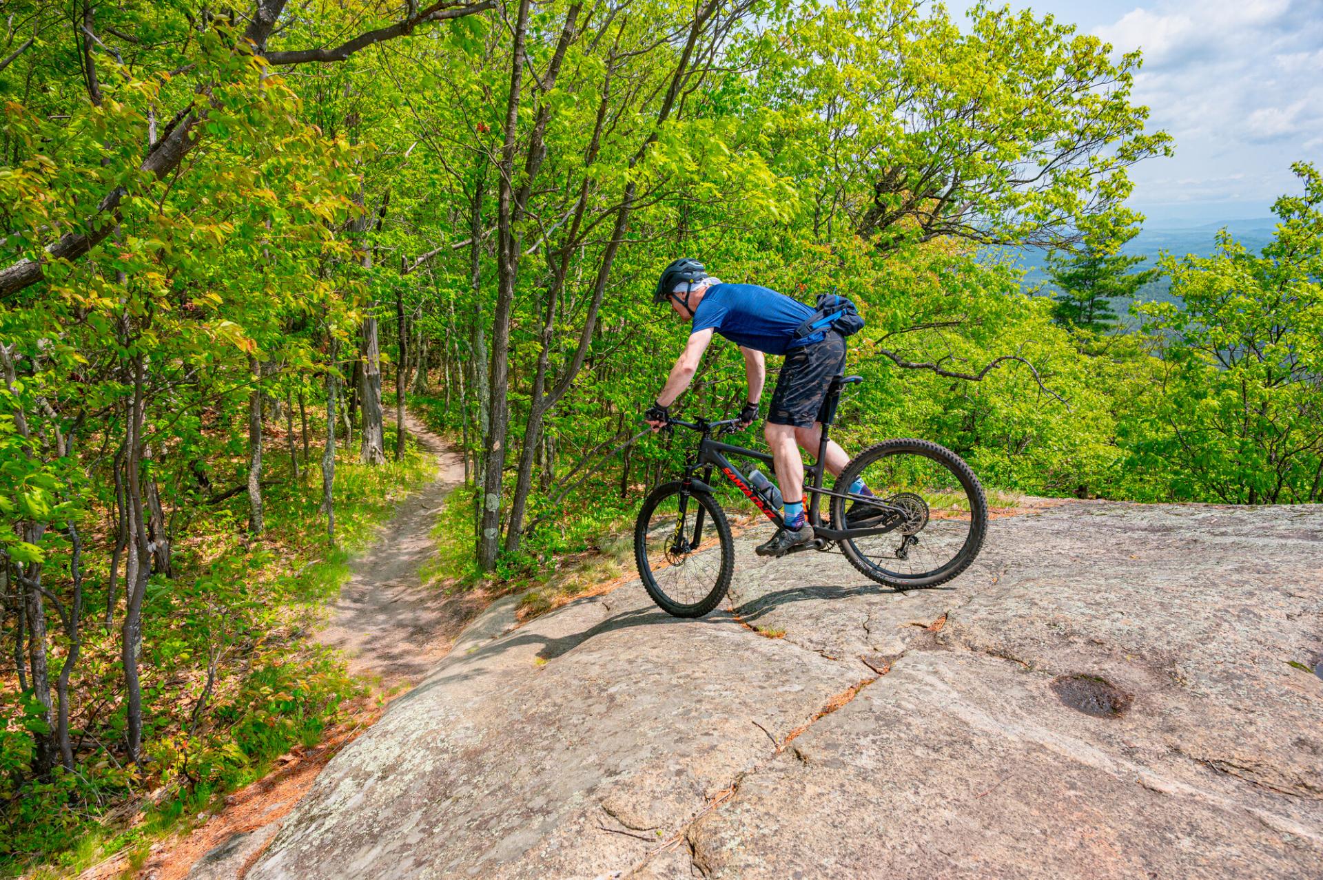 A mountain biker goes down a rock slab towards a single track trail