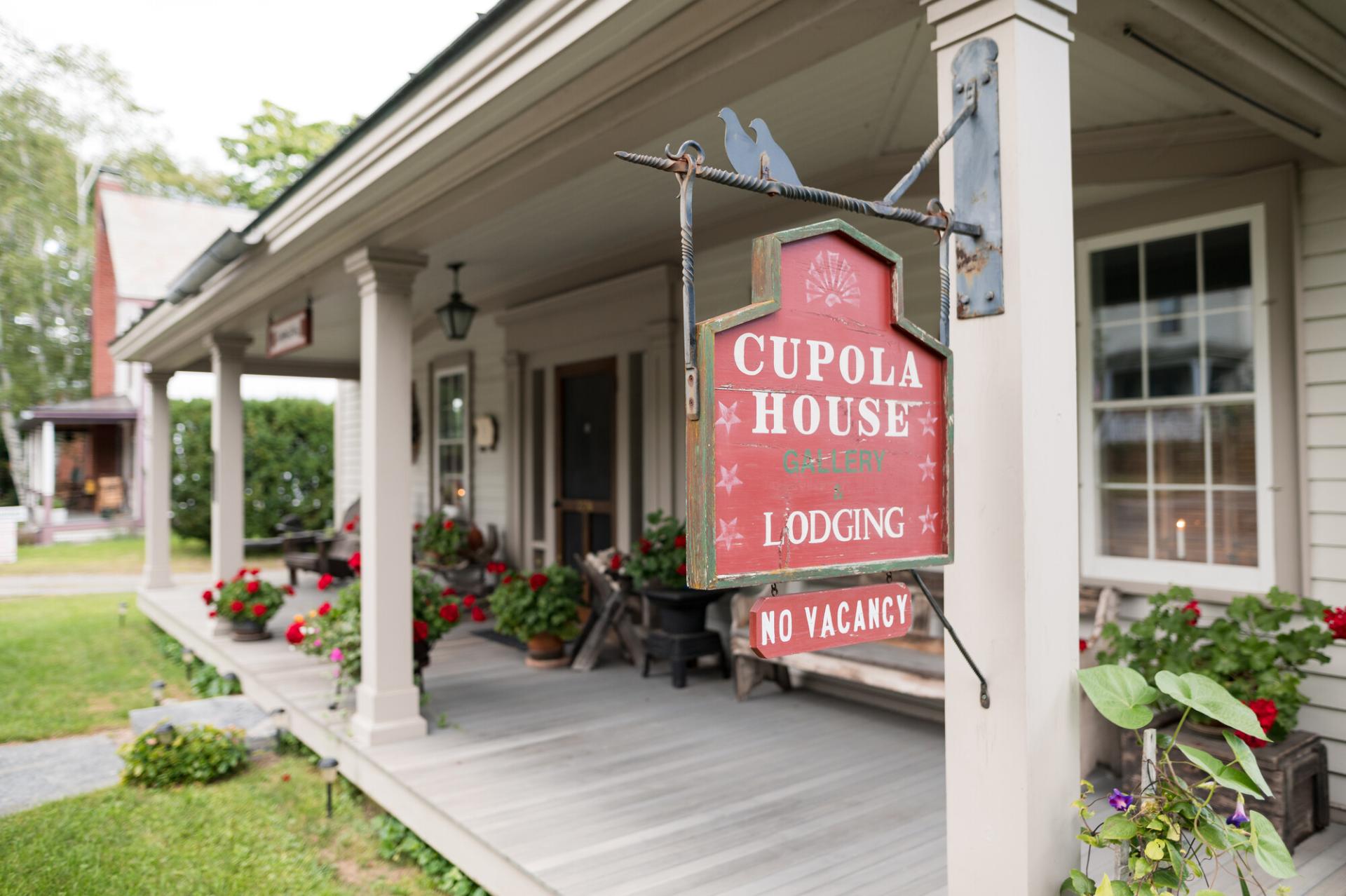 A red sign hanging off the post of a covered porch for Cupola House Lodging.