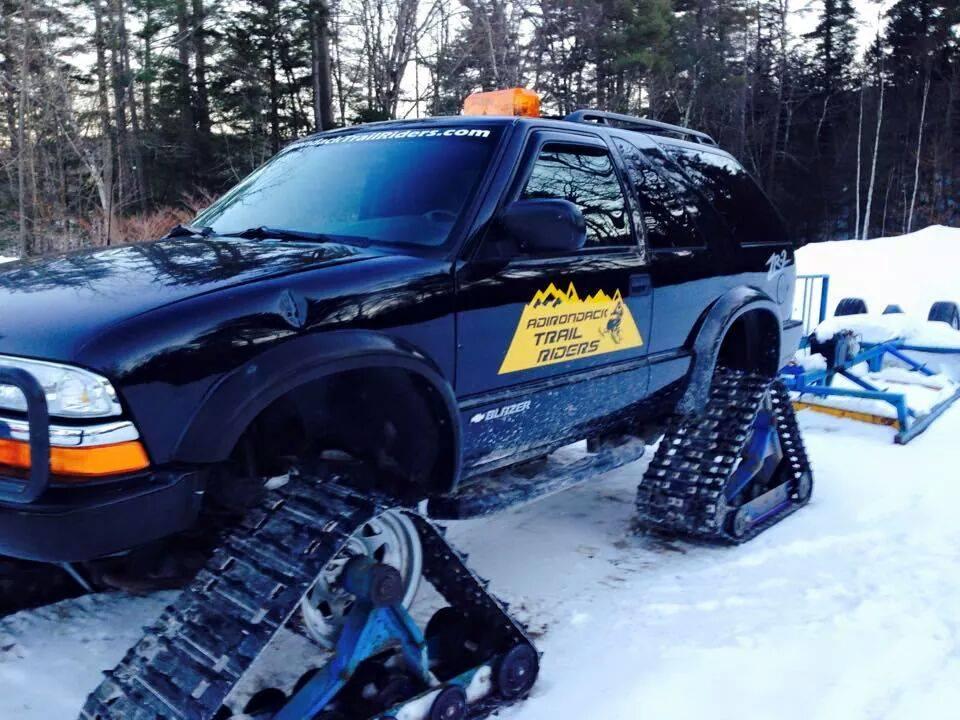 A modified SUV with tracks instead of wheels with a yellow decal for the Adirondack Trail Riders.