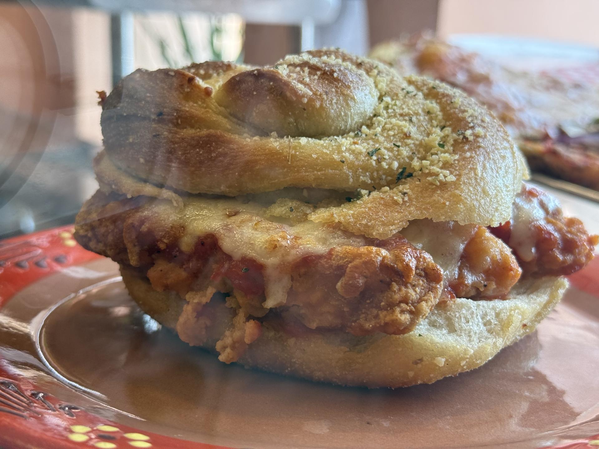 A chicken cutlet with cheese and sauce on a  giant garlic knot sandwich.