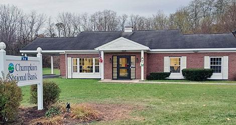 A squat brick building with white trim and covered entry way with large lawn.