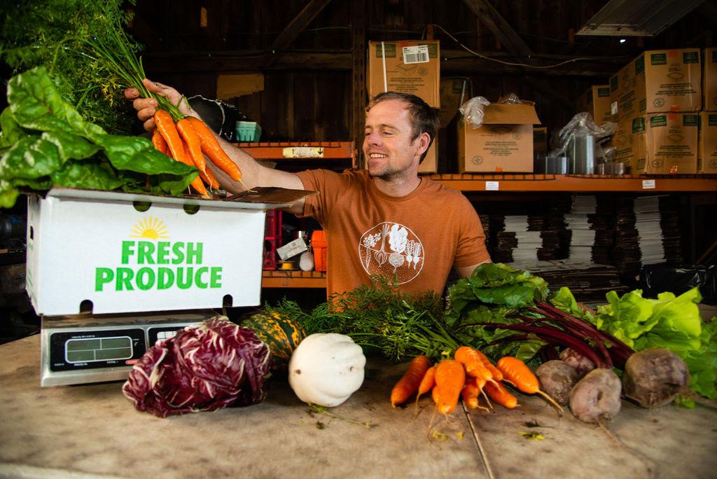A man at a farm stand weighs a bundle of carrots.