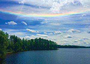 The view from a mountain top looking over the pine trees with a sea of clouds and a rainbow above.