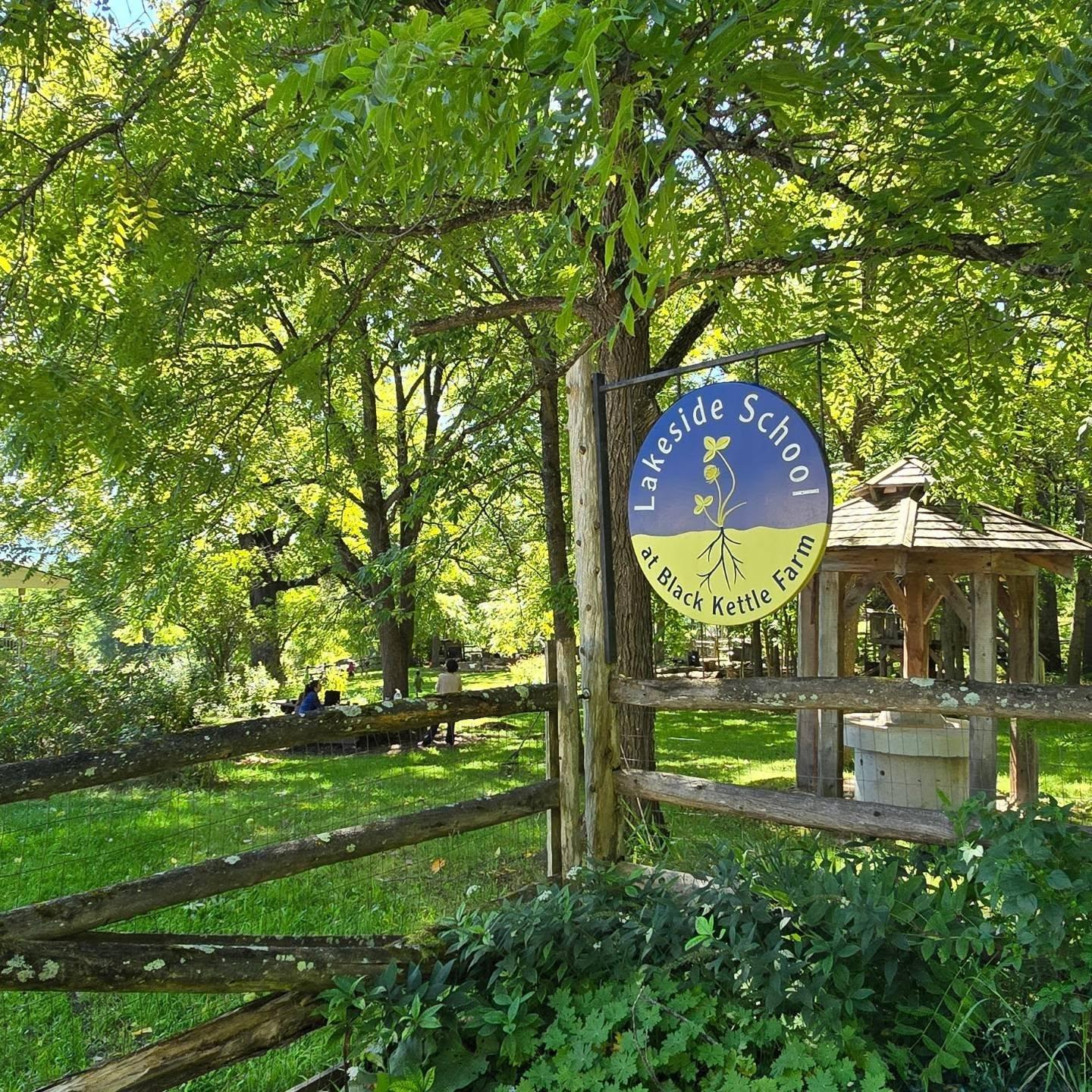 A lush green landscape where a round sign for Lakeside School at Black Kettle Farm.