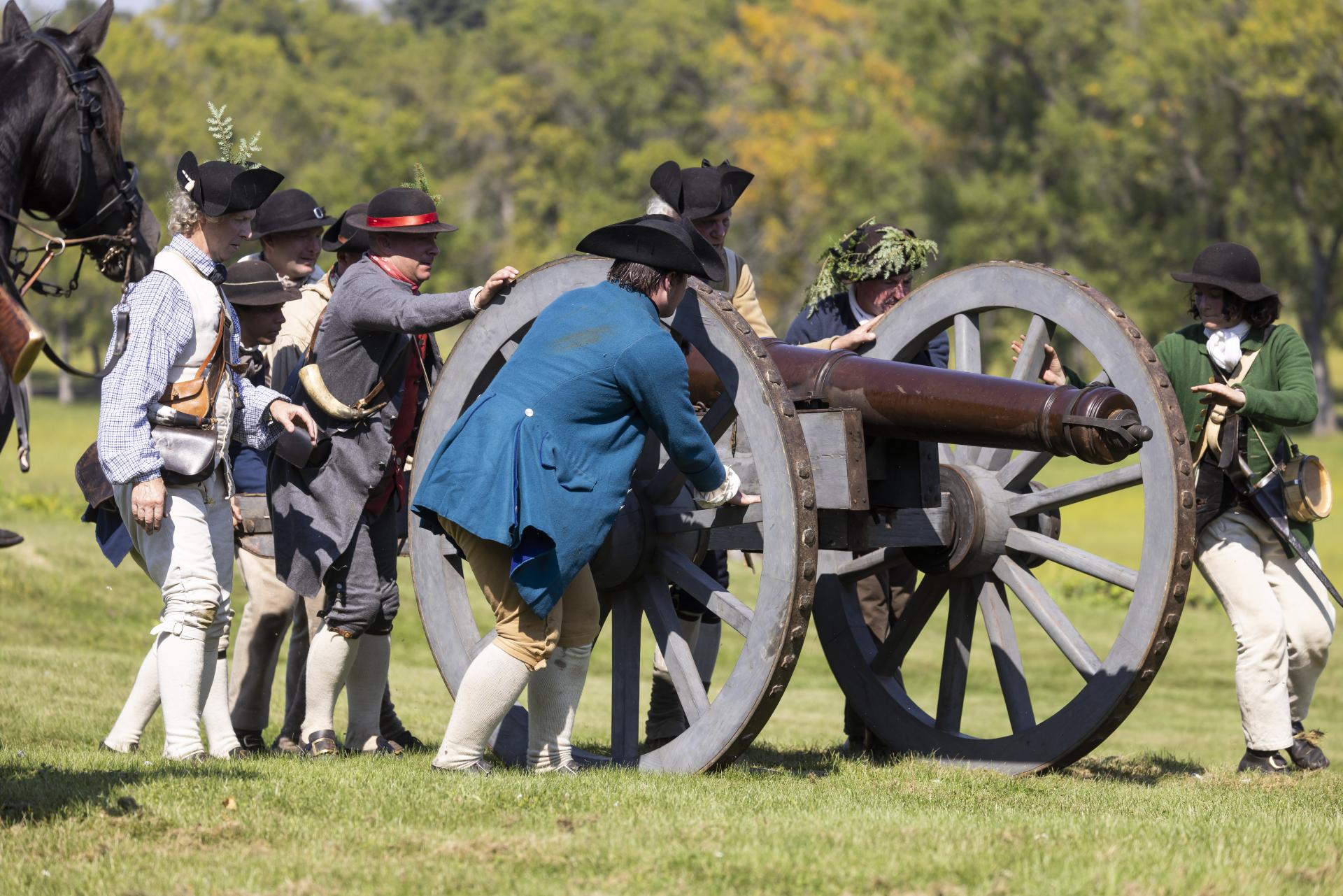 Reenactment actors in period correct clothing demonstrate a cannon firing.