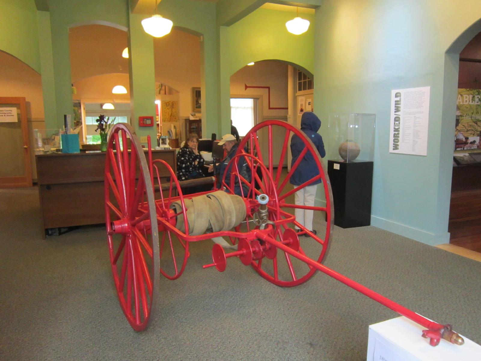 A red fire hose reel on large wagon wheels.