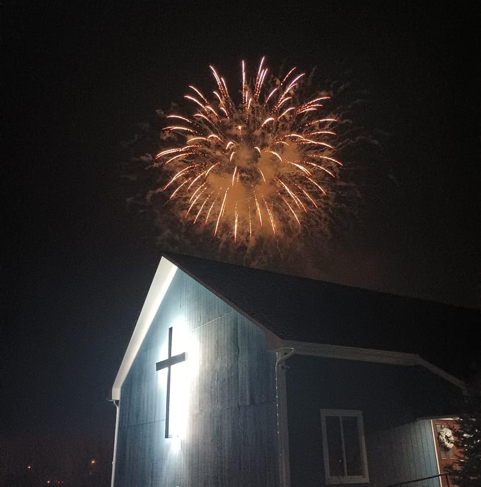 An illuminated cross on the side of a building with a firework exploding above.