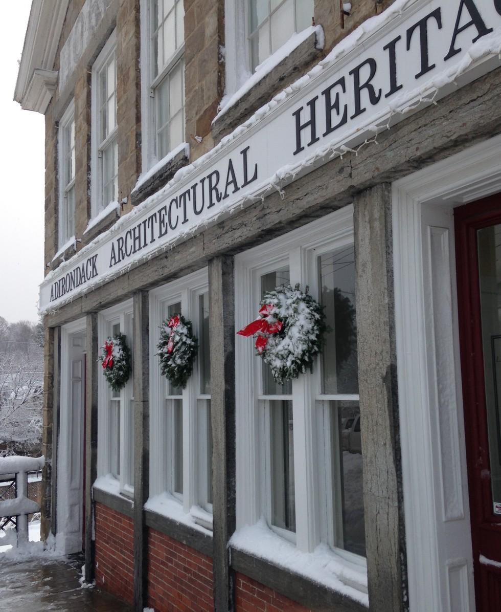 A tall stone building with white trim and winter wreaths with red bows that houses the Adirondack Architectural Heritage.