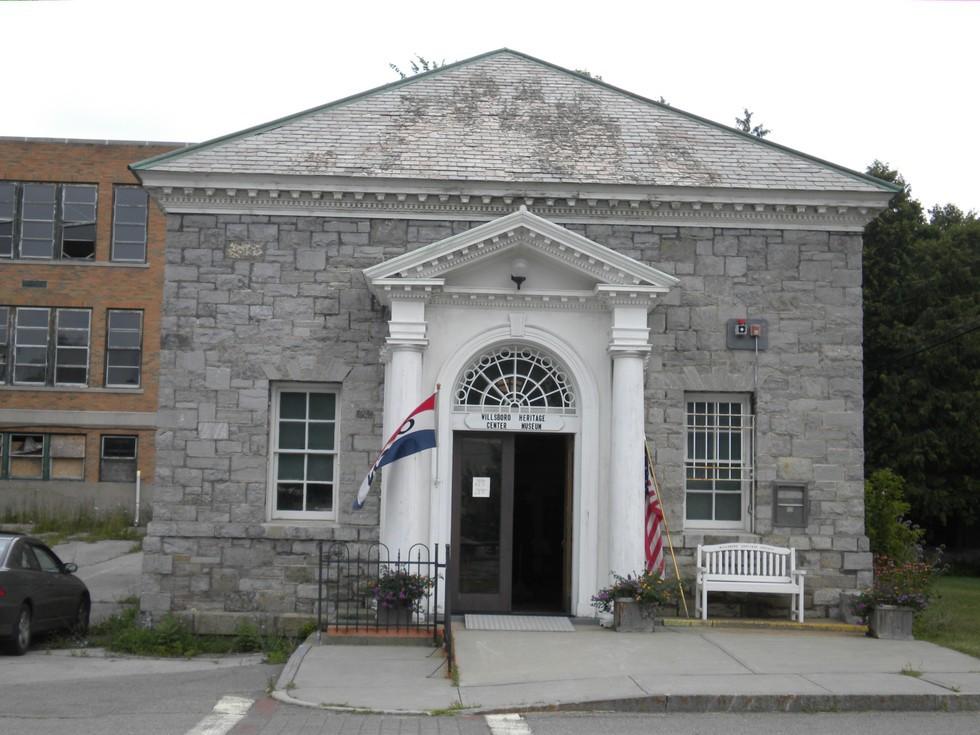 A stone building with white columns supporting the covered entry roof.