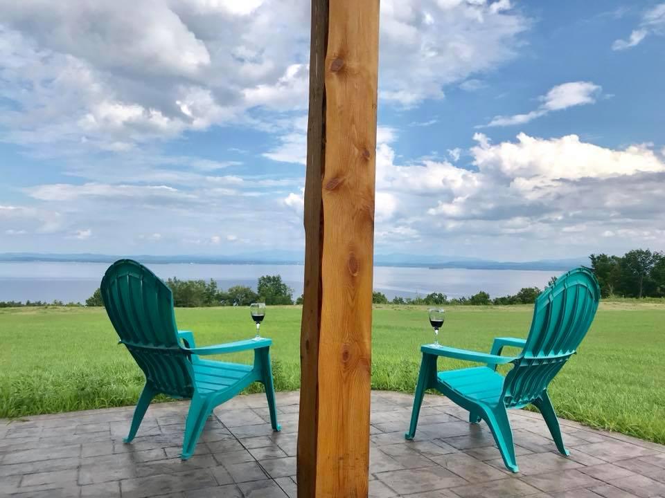 Two Adk chairs with wineglasses on arm overlooking Lake Champlain