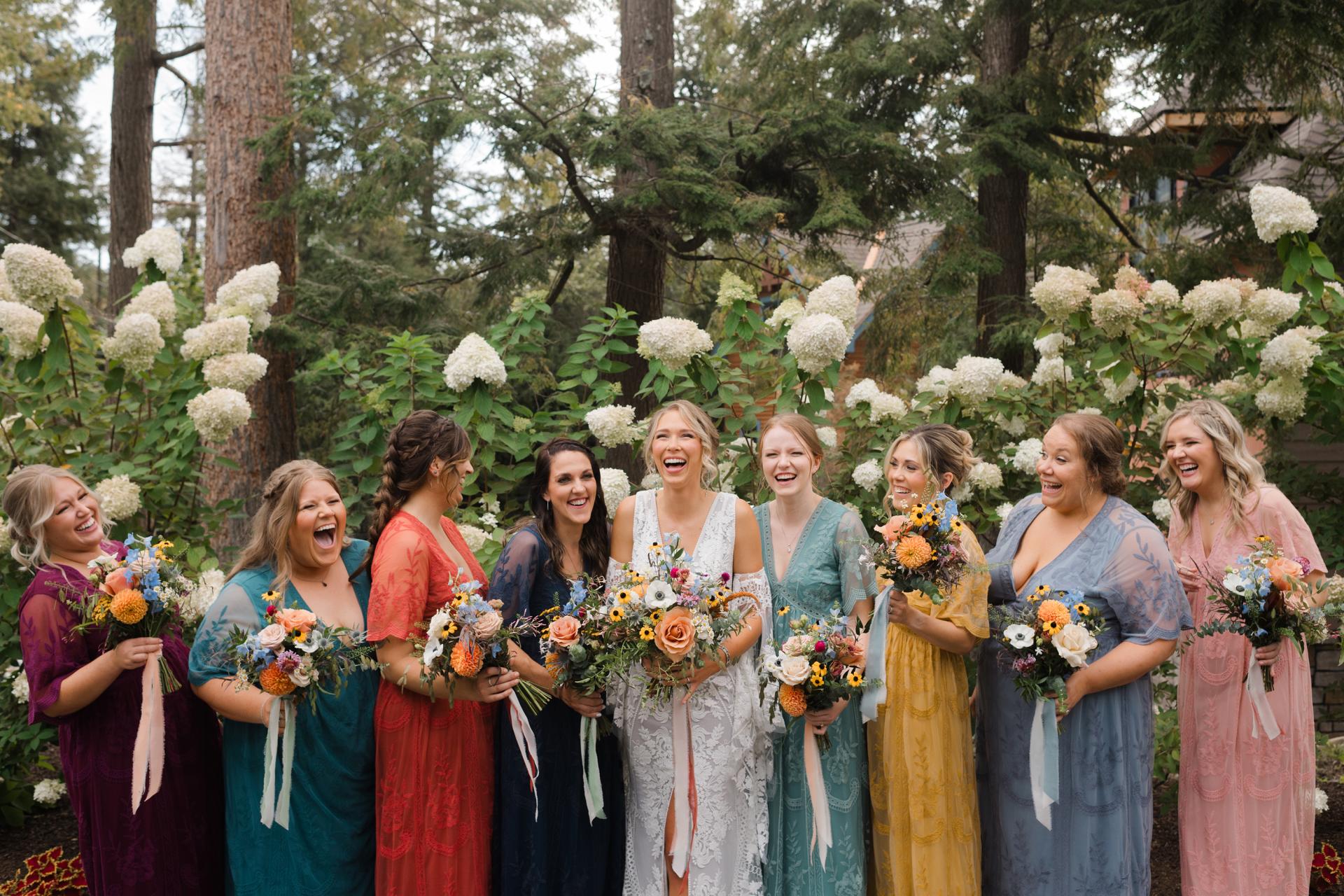 The bridal party hold colorful bouquets while wearing colorful dresses.