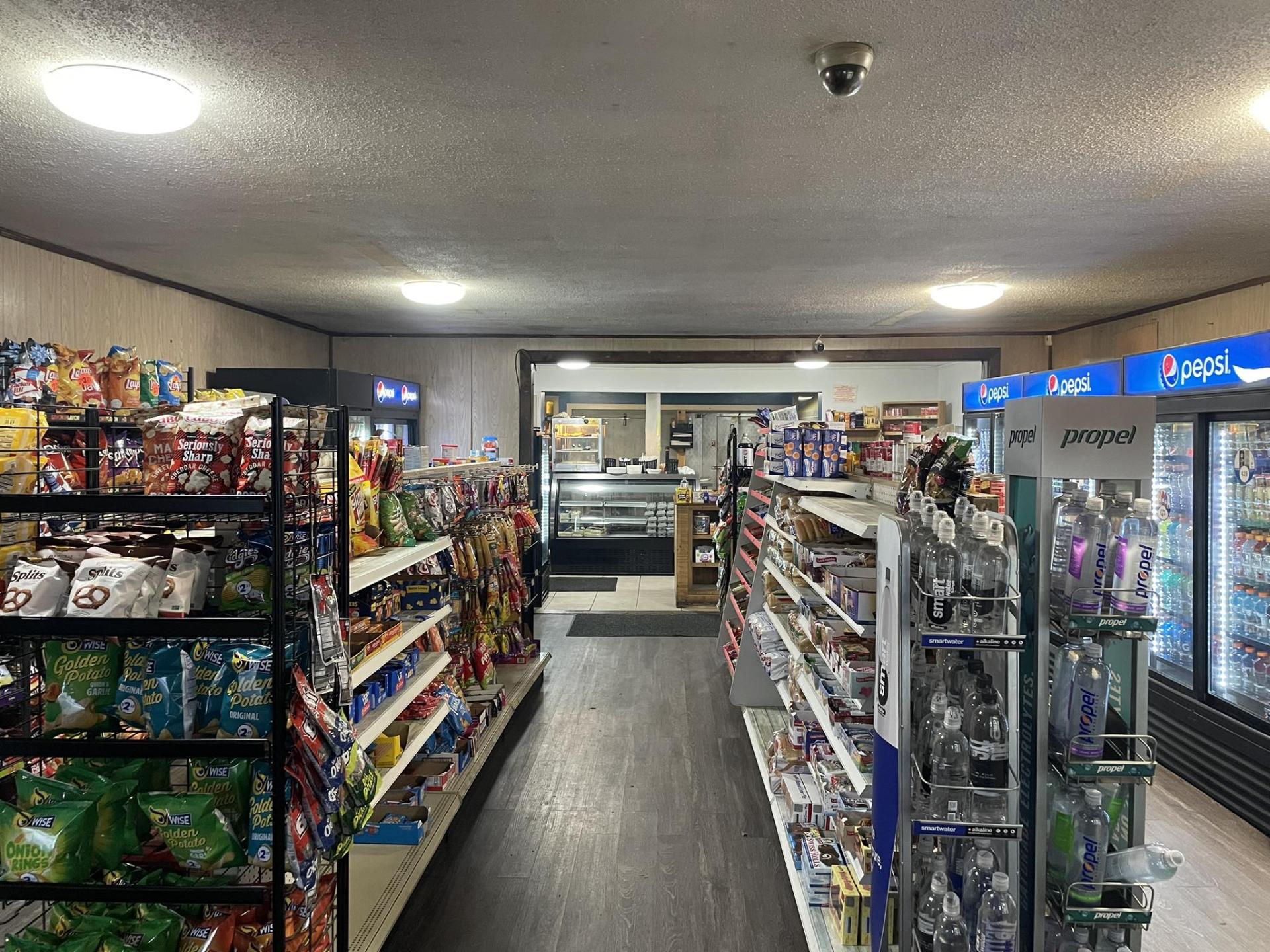 Shelves of snacks and cold drinks in coolers leading to the deli counter at Grover Hills Deli
