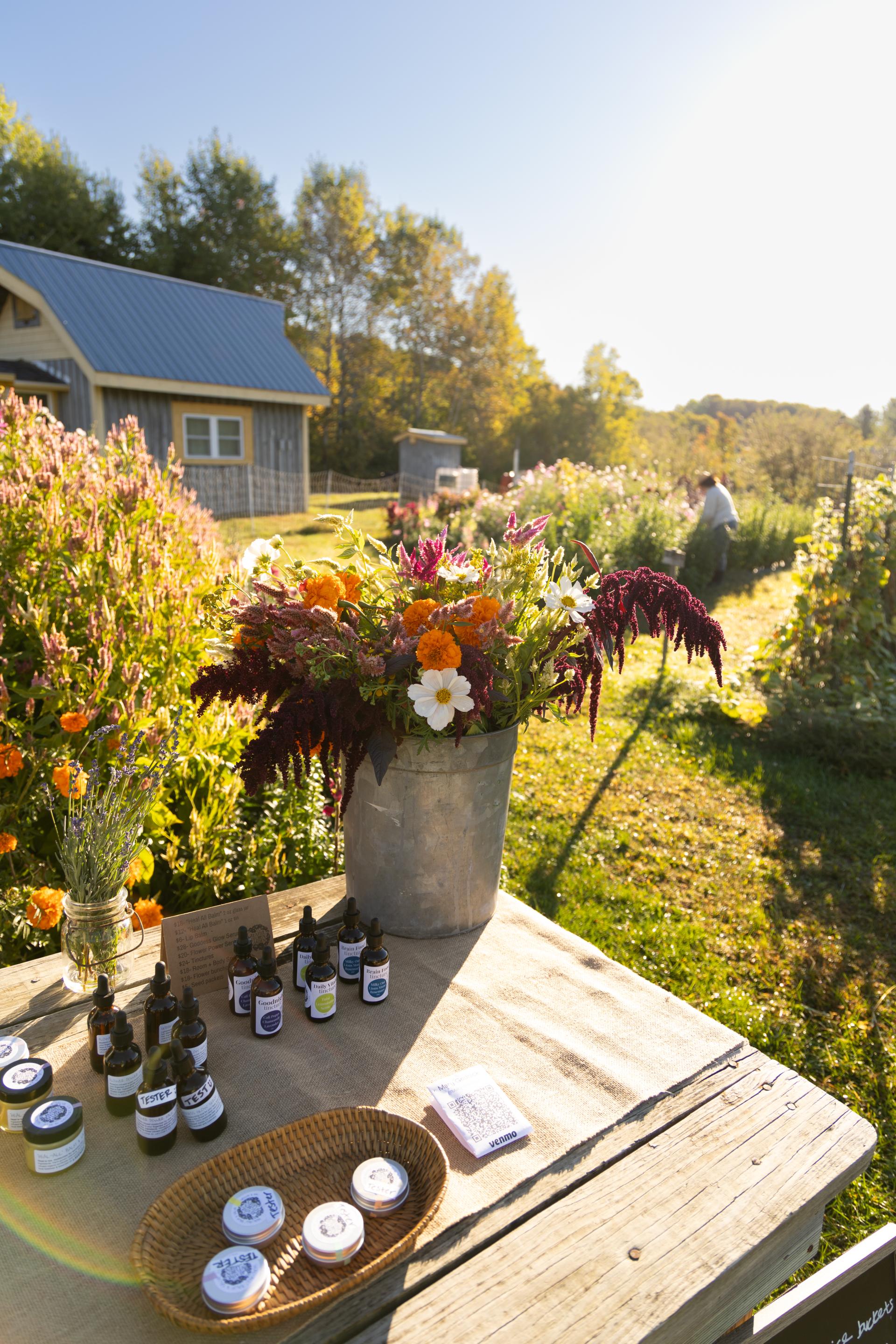 A bucket of flowers sit on a table with tinctures and salves displayed.