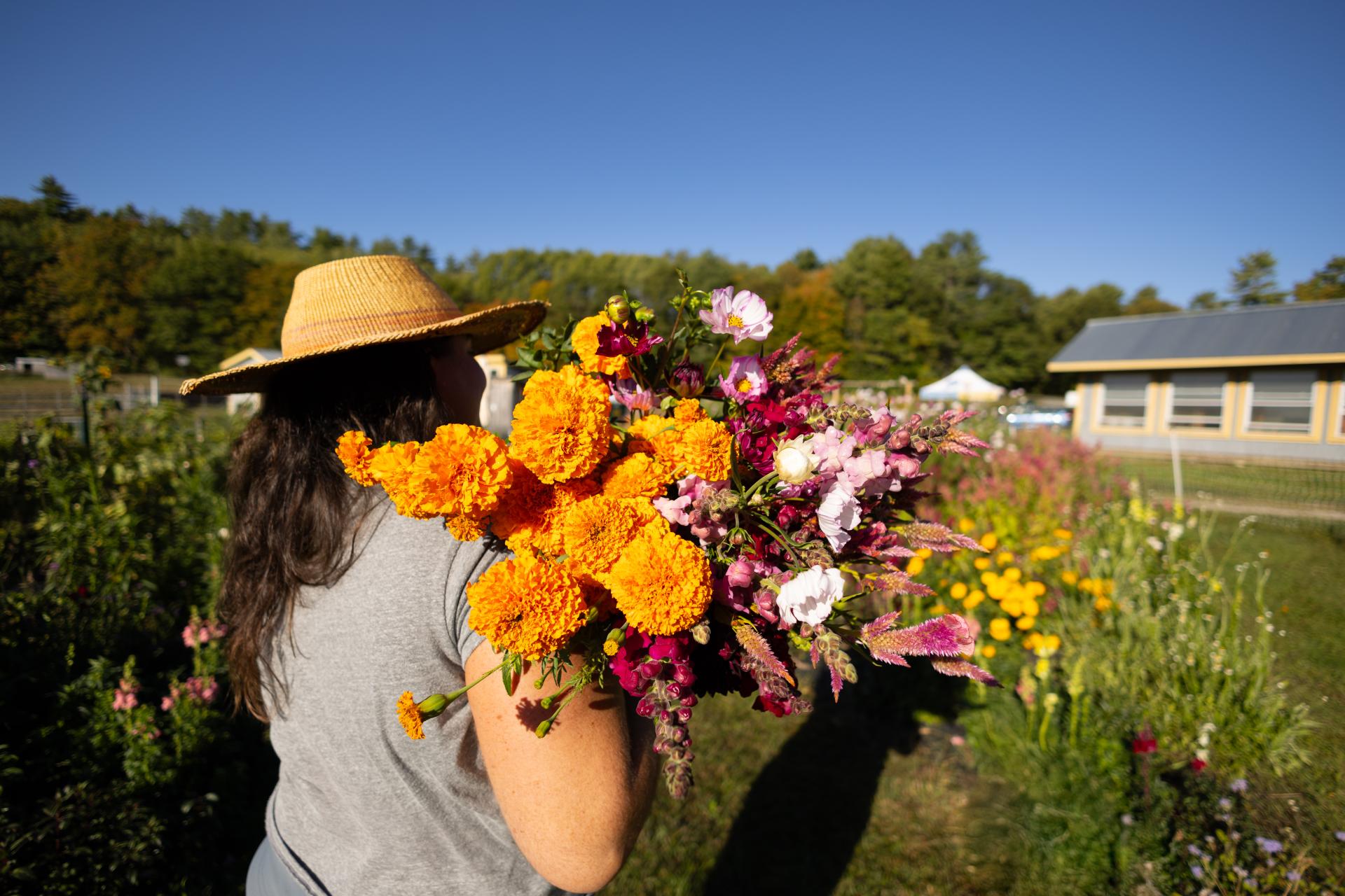 A woman in a straw hat holds a bouquet of orange and pink flowers over her shoulder.