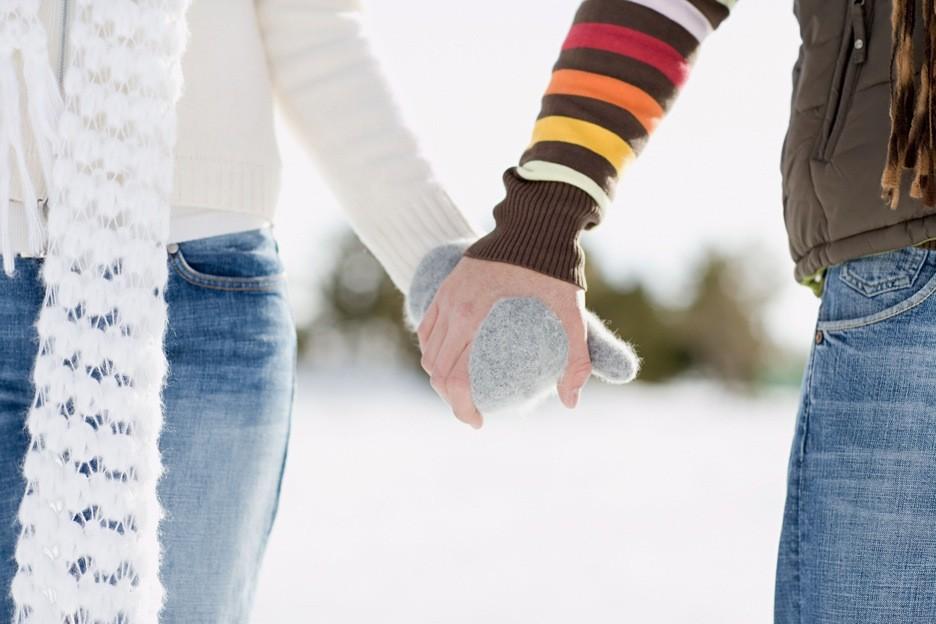 Two people holding gloved hands and walking in the snow