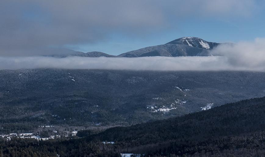 A tall mountain pokes through clouds in the winter