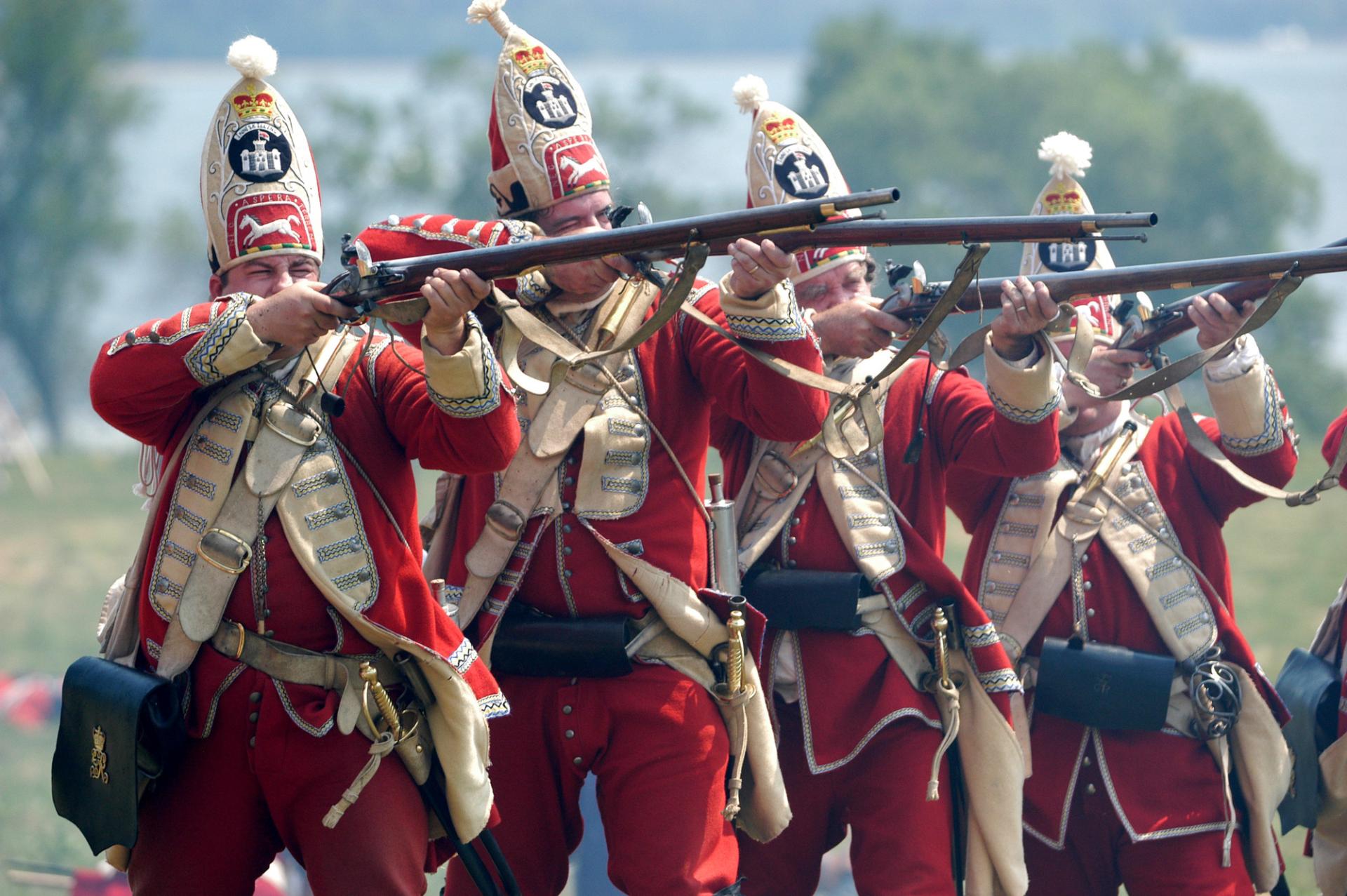 Men in period military costume fire muskets during a reenactment.