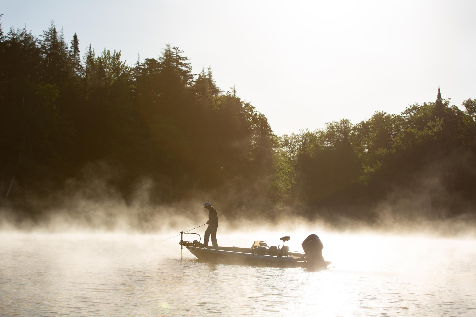 A angler fishing off a boat in the morning mist.