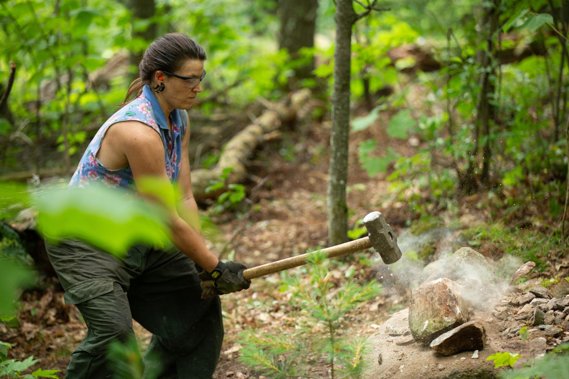 A woman breaks up a stone with a large hammer