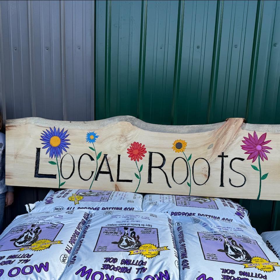 A live edge slab with Local Roots painted on it with colorful flowers